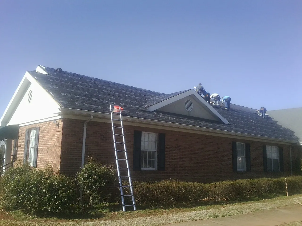 Crew tearing shingles off a brick ranch roof with a ladder set — Emergency Roof Repair work by our crew in Hiawatha