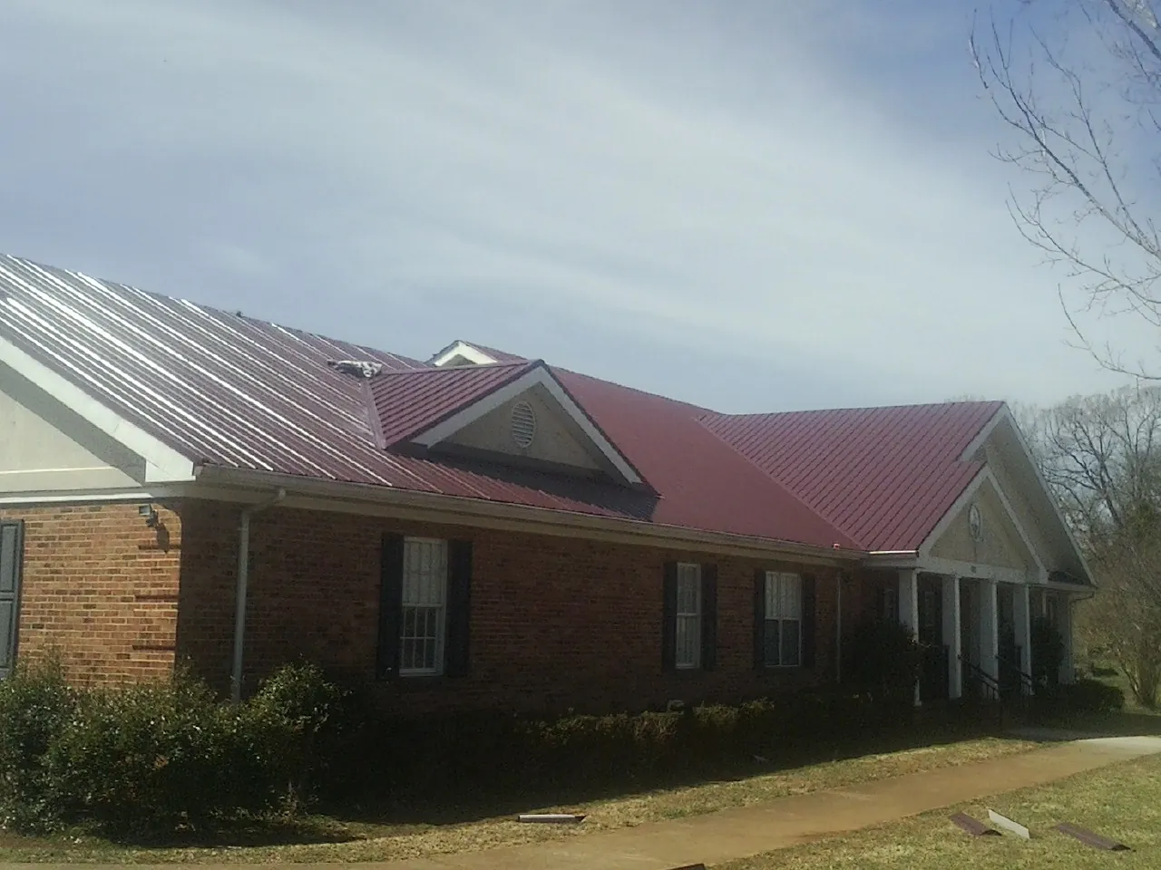 Red metal roof with gabled entries on a long brick building, from a Hail Damage Roof Repair job in Hiawatha