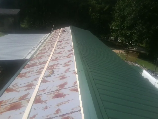 Old rusted panels beside newly installed green metal roofing — Wind Damage Roof Repair by Roofing Brothers in Hiawatha