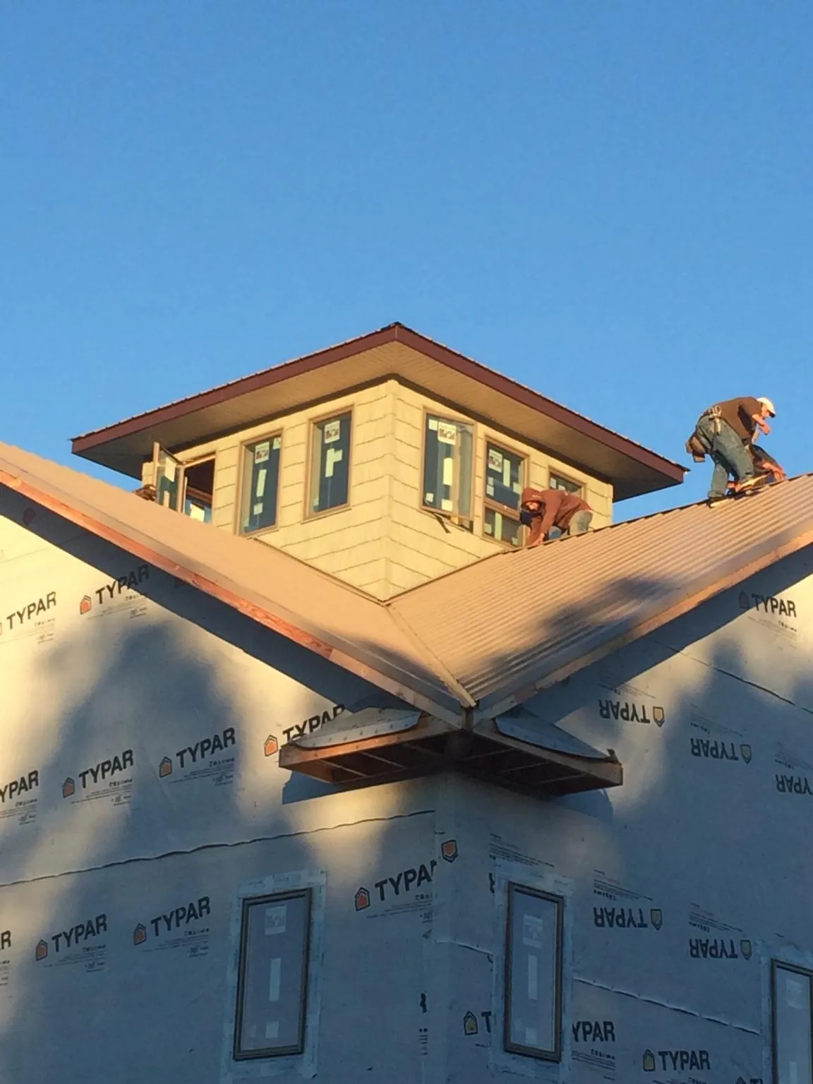 Roofers working around a rooftop cupola on a new metal roof at sunset — Roof Waterproofing in Hiawatha by Roofing Brothers